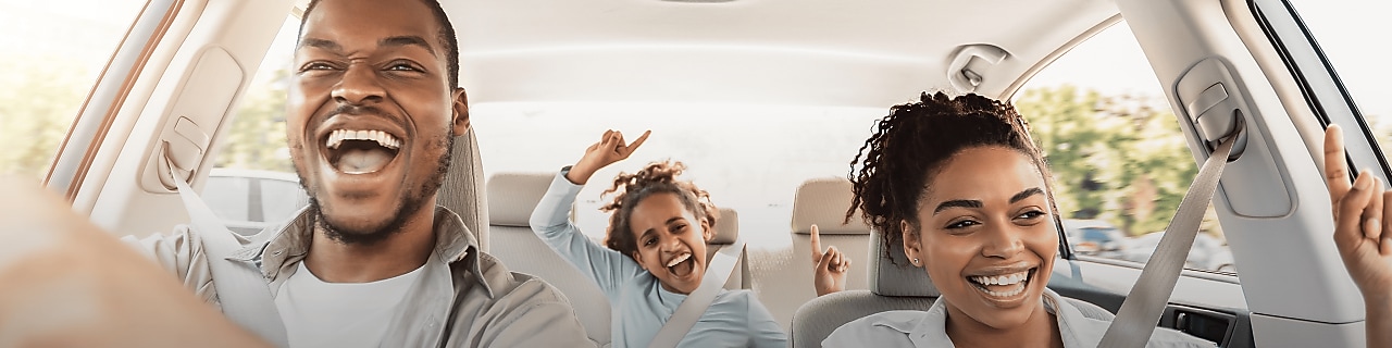 A happy, smiling family in a car, with a child seated in the rear seat, enjoying a safe and comfortable journey.