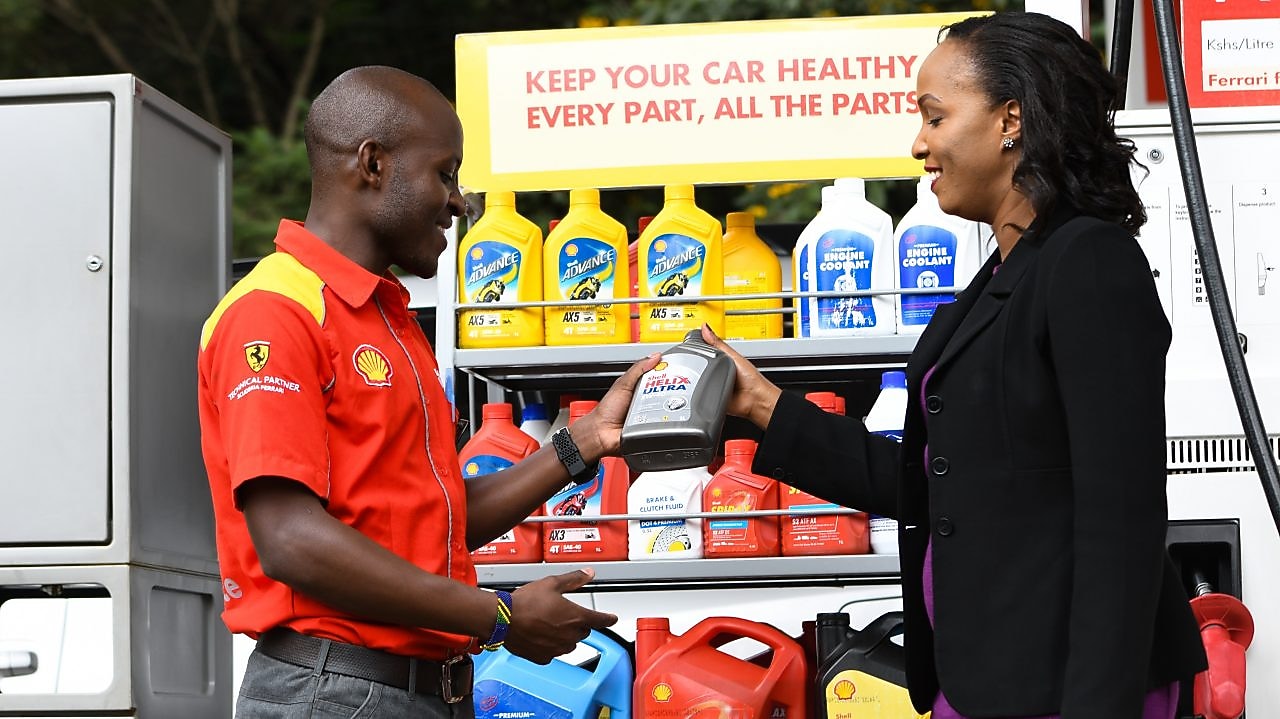 A red Ferrari sitting on a Shell station forecourt with a man leaning on a petrol pump