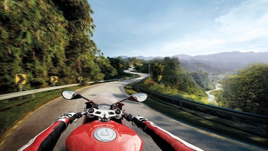 A motorcyclist’s perspective riding through a scenic mountain route, symbolizing smooth engine performance with Shell lubricants.