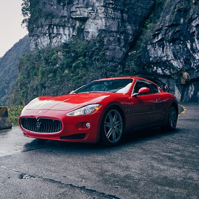 A red Maserati driving up a scenic mountain road, highlighting premium engine care.