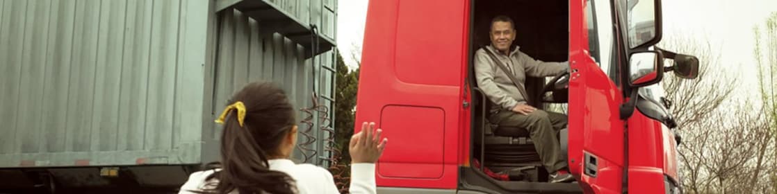 Man in red truck cab with door open waving to his daughter