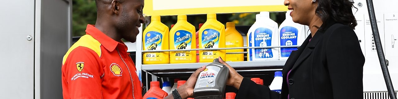 A red Ferrari sitting on a Shell station forecourt with a man leaning on a petrol pump